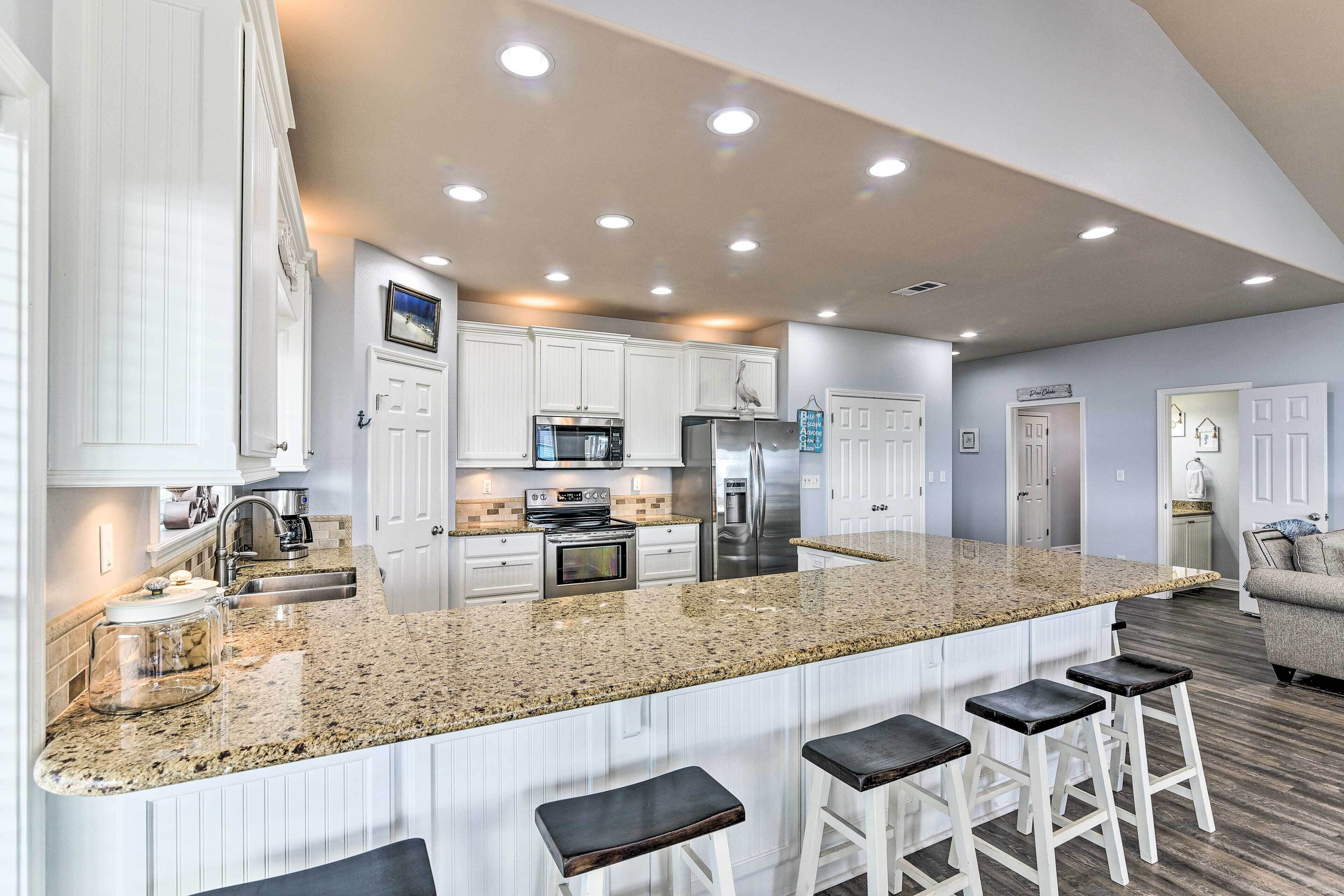A modern kitchen with white cabinets, granite countertops, and stainless steel appliances. There are three bar stools and a large island.