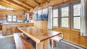 A wooden cabin interior with a large dining table, benches, a kitchen area, and large windows. - Treehouse-style Cabin, 1 Mi to Massanutten Resort (McGaheysville)