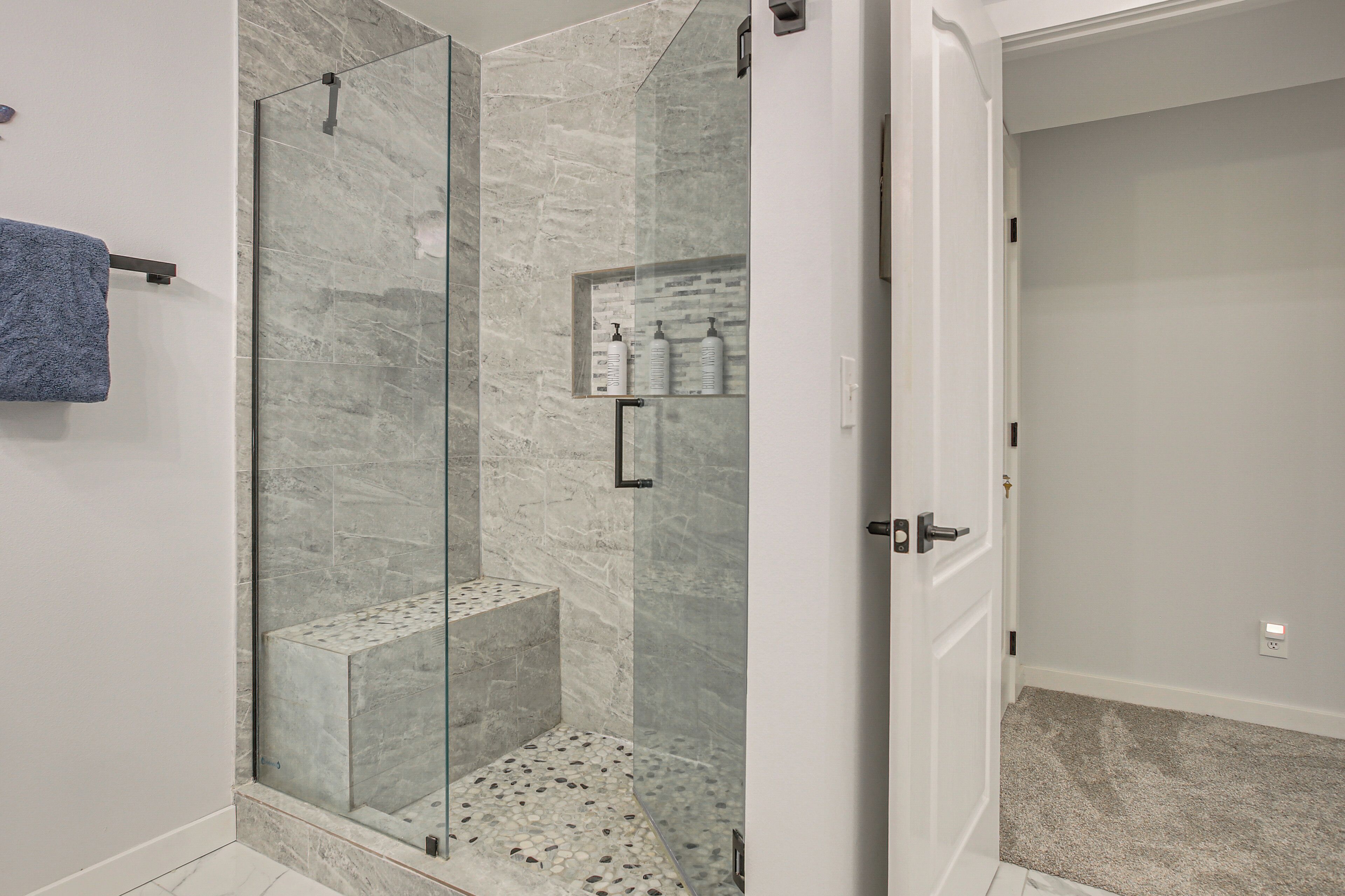 Un baño moderno con ducha envuelta en vidrio, paredes de mármol y un toallero a la vista.