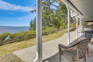 A covered outdoor area with a view of the water, a concrete path, and a chair. - Waterfront PNW Escape w/ Deck & Beach Access! (Port Hadlock)