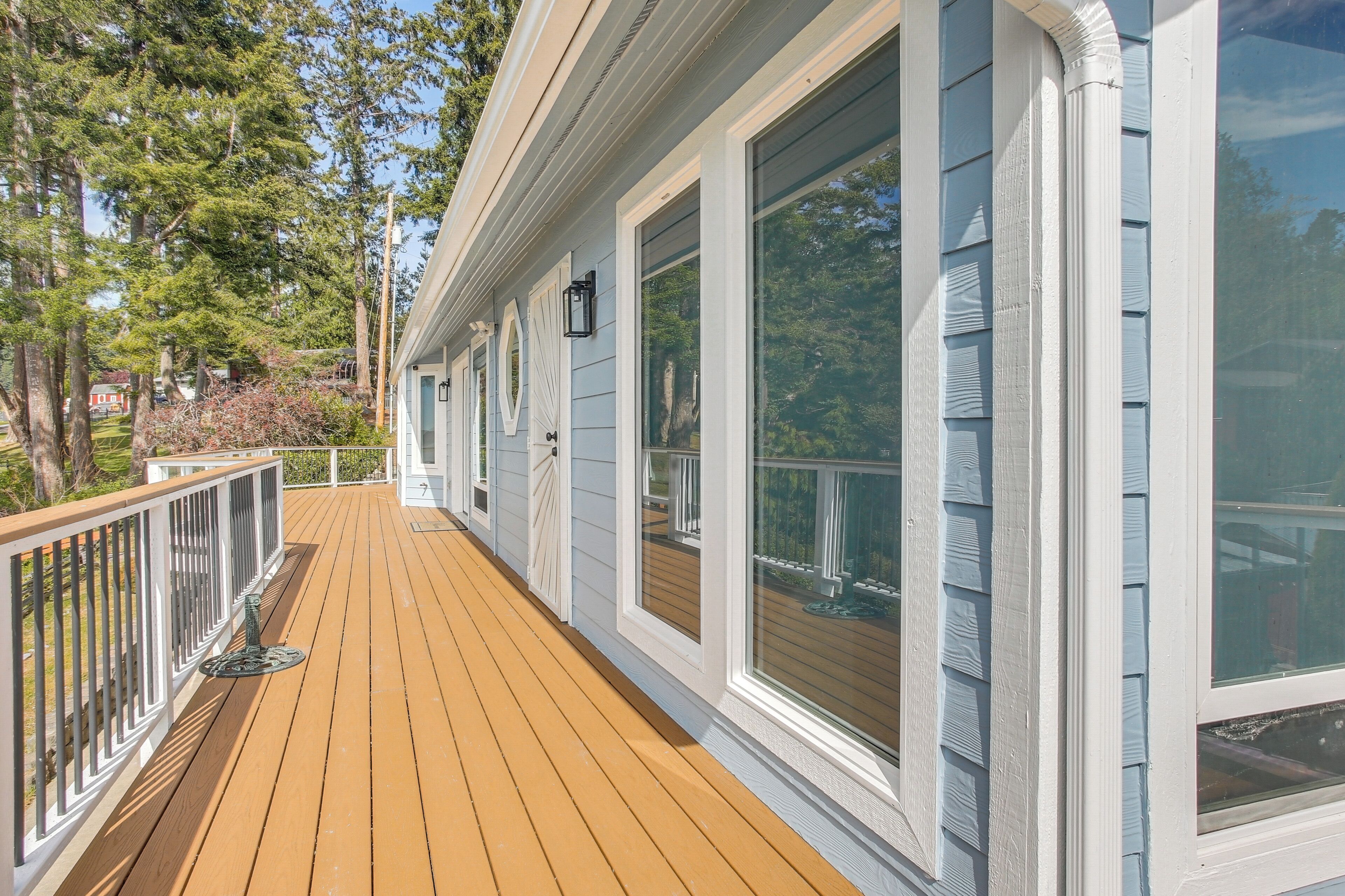 A wooden deck with white railings, large windows, and a view of trees.