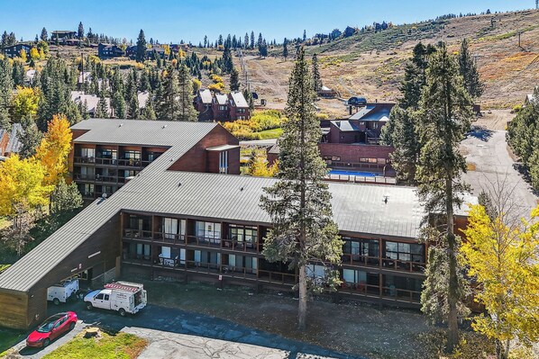 Un edificio de varios pisos con techo plano, rodeado de árboles y un paisaje montañoso.