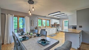 Une cuisine moderne avec des meubles blancs, un plan de travail en bois et un coin repas avec une table dressée pour quatre personnes.