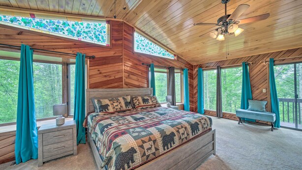 Une chambre dans une cabane en bois, avec un grand lit, une table de chevet, un banc et un ventilateur de plafond.