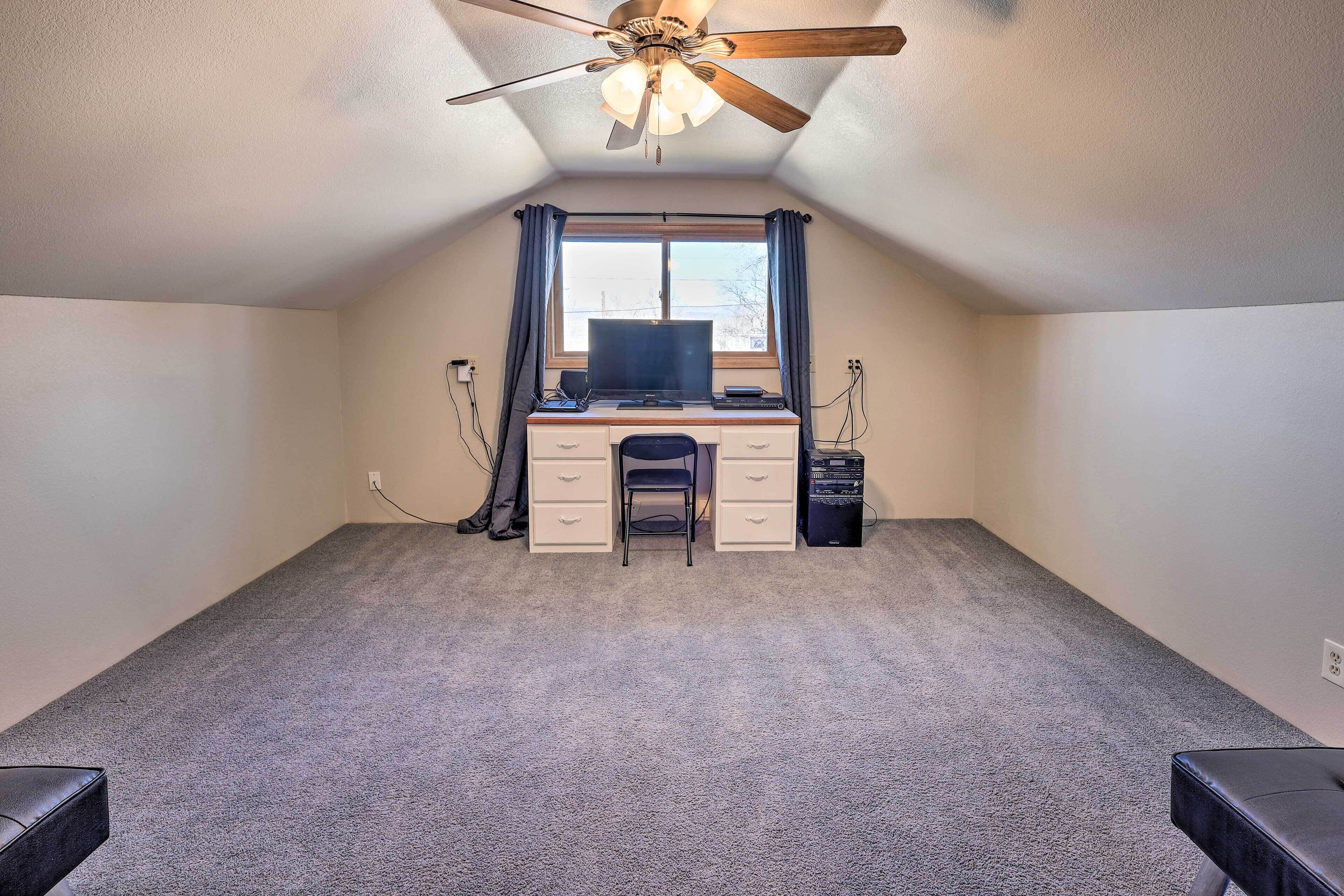 Une petite pièce, recouverte de moquette, avec un bureau, une chaise et un ventilateur de plafond.