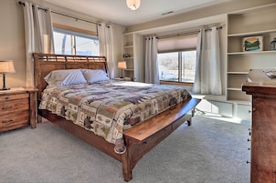Un dormitorio con cama de madera, una mesita de noche, un banco y una estantería empotrada.