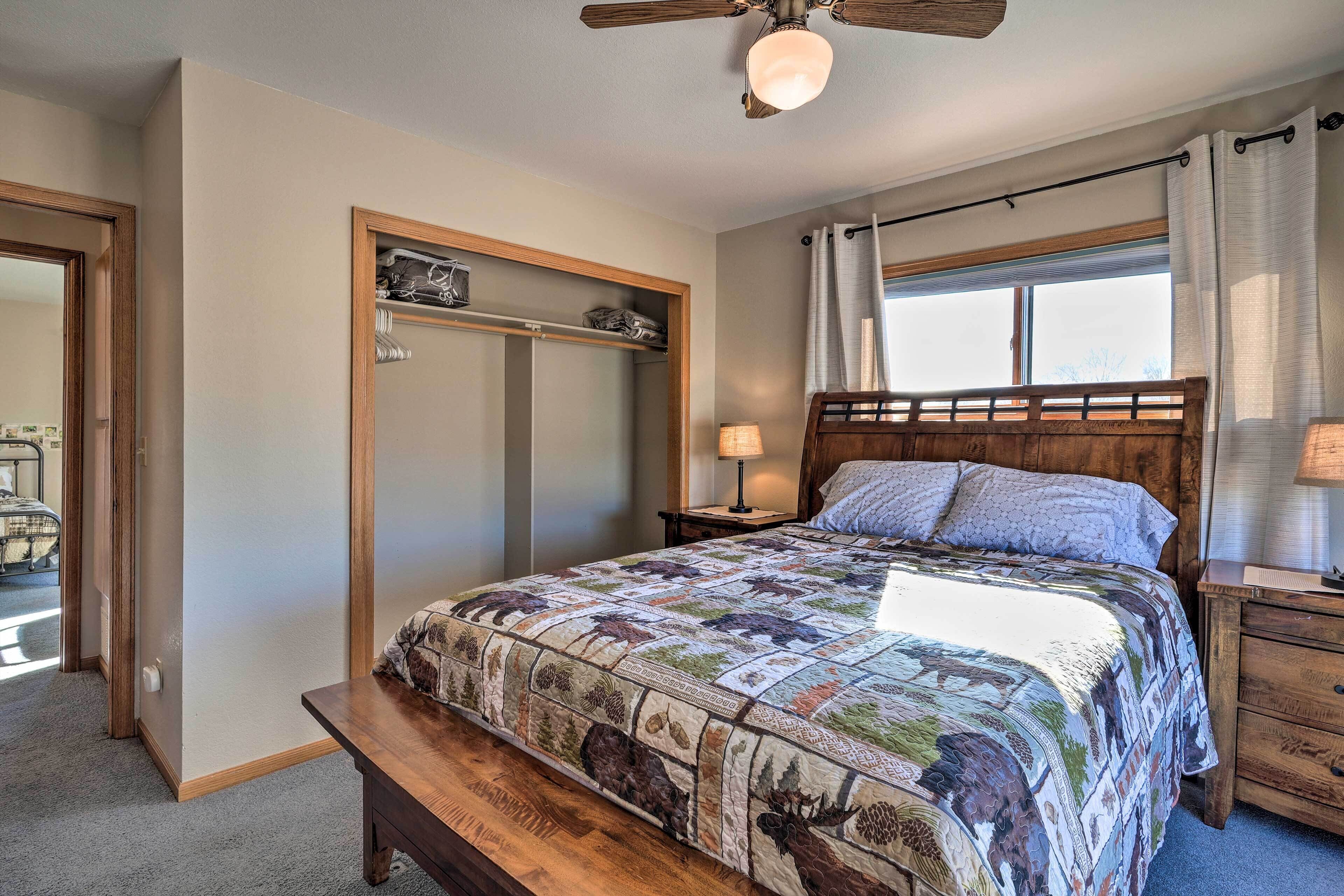Une chambre à coucher avec un grand lit, une tête de lit en bois, une table de chevet, une lampe de chevet, une fenêtre avec des rideaux, un ventilateur de plafond et un banc en bois.