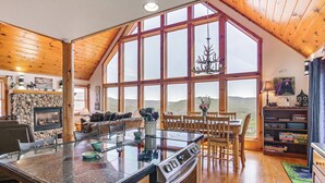 A spacious kitchen with a large island, wooden ceiling, and a view of the mountains through large windows. - West Virginia Cabin Near Snowshoe Mountain Resort (Slaty Fork)