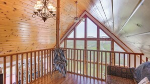 A wooden interior with a high ceiling, a chandelier, a view through large windows, a wooden railing, and a patterned sofa. - West Virginia Cabin Near Snowshoe Mountain Resort (Slaty Fork)