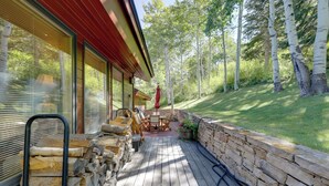 Una terraza de madera con muros de piedra, muebles de exterior y un paraguas rojo.