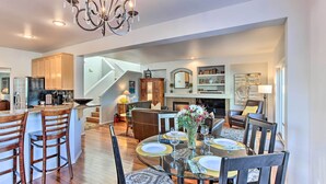A spacious living area with a dining table set for four, a kitchen with wooden cabinets, and a staircase leading to another level.