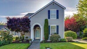 A two-story house with a front entrance, a well-maintained lawn, and various shrubs and trees.