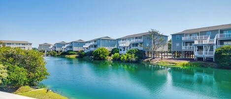 A residential area with multi-story buildings, a clear blue sky, and a calm body of water.