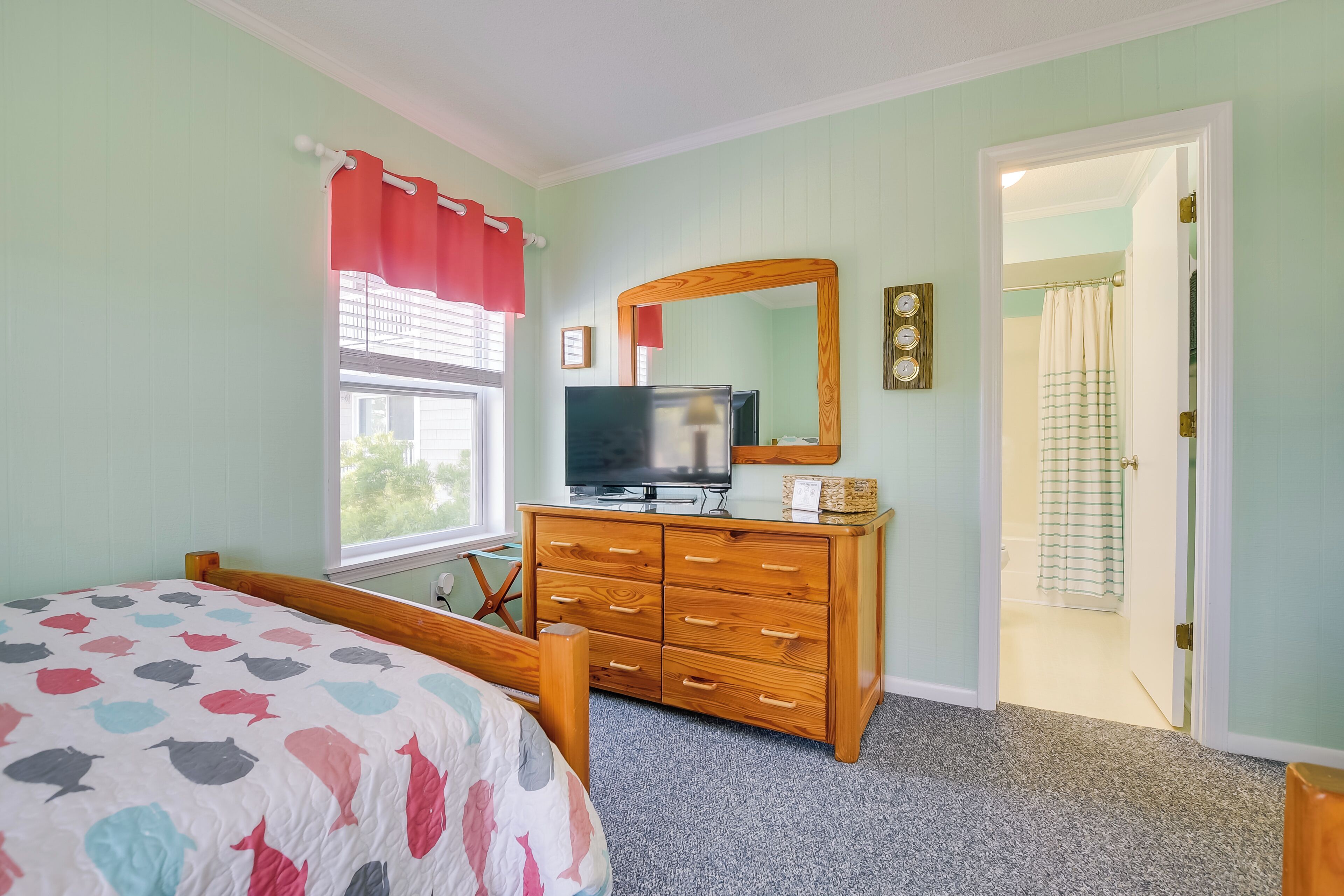 A bedroom with a bed, dresser, television, and a door leading to a bathroom.