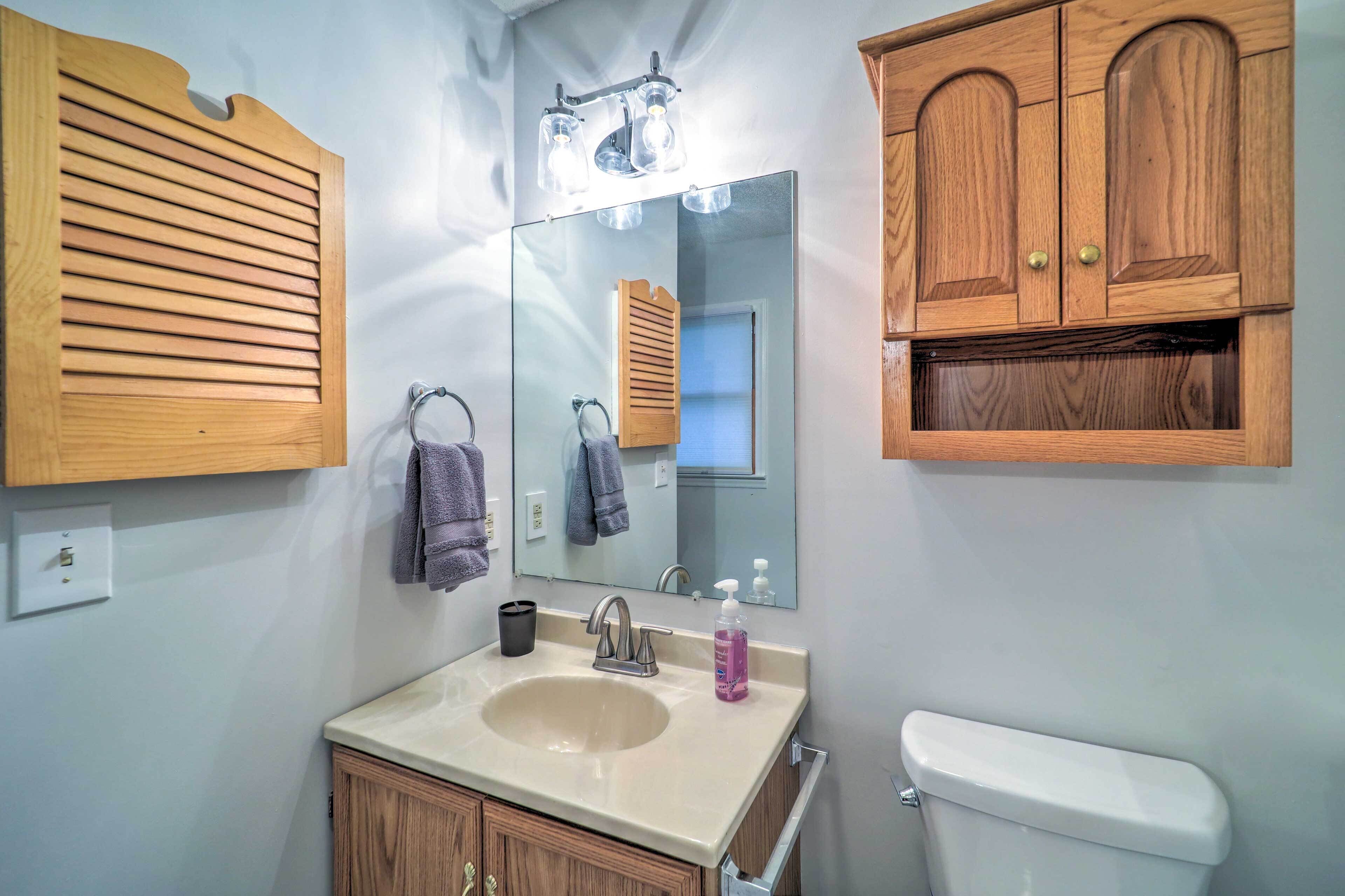 A bathroom with a sink, mirror, wooden cabinets, and a toilet.