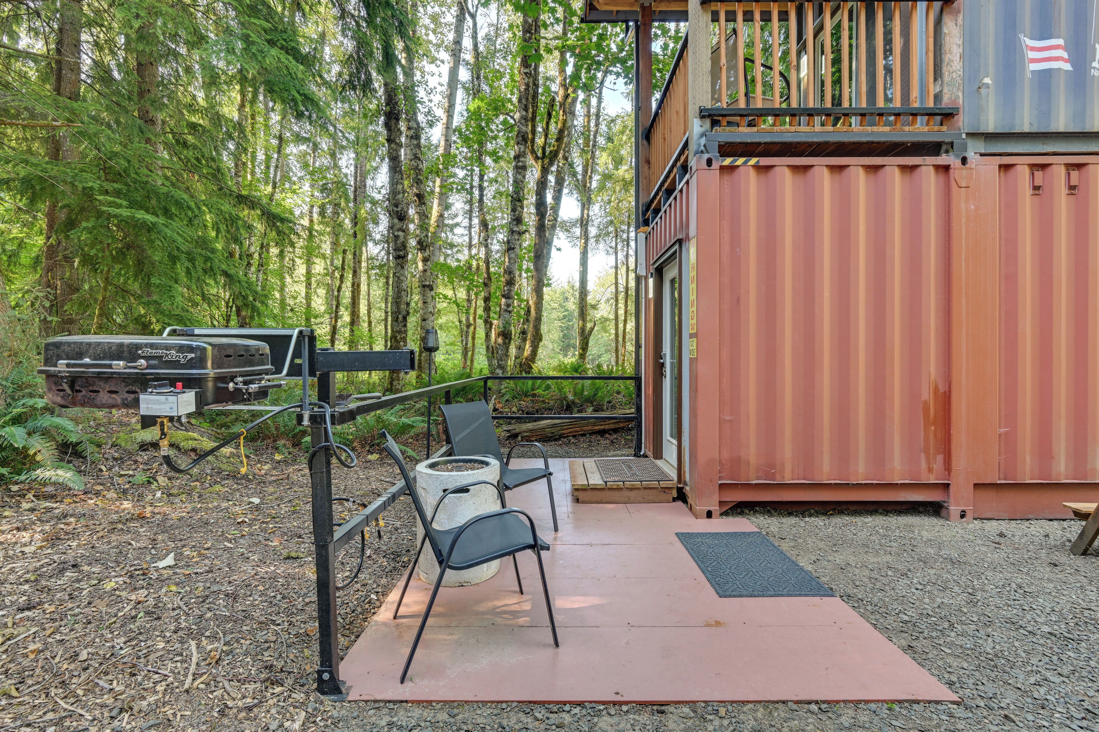 Una cabaña rústica con terraza, mobiliario exterior y una parrilla.