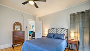 Un dormitorio con cama, cómoda, mesita de noche, ventilador de techo y puerta que da a otra habitación.