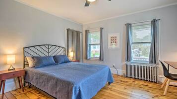 A bedroom with a bed, a nightstand, a desk, and a window with curtains.