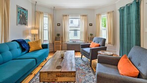 Un salón con un sofá azul, un sillón gris, una mesa de centro de madera y una alfombra estampada.