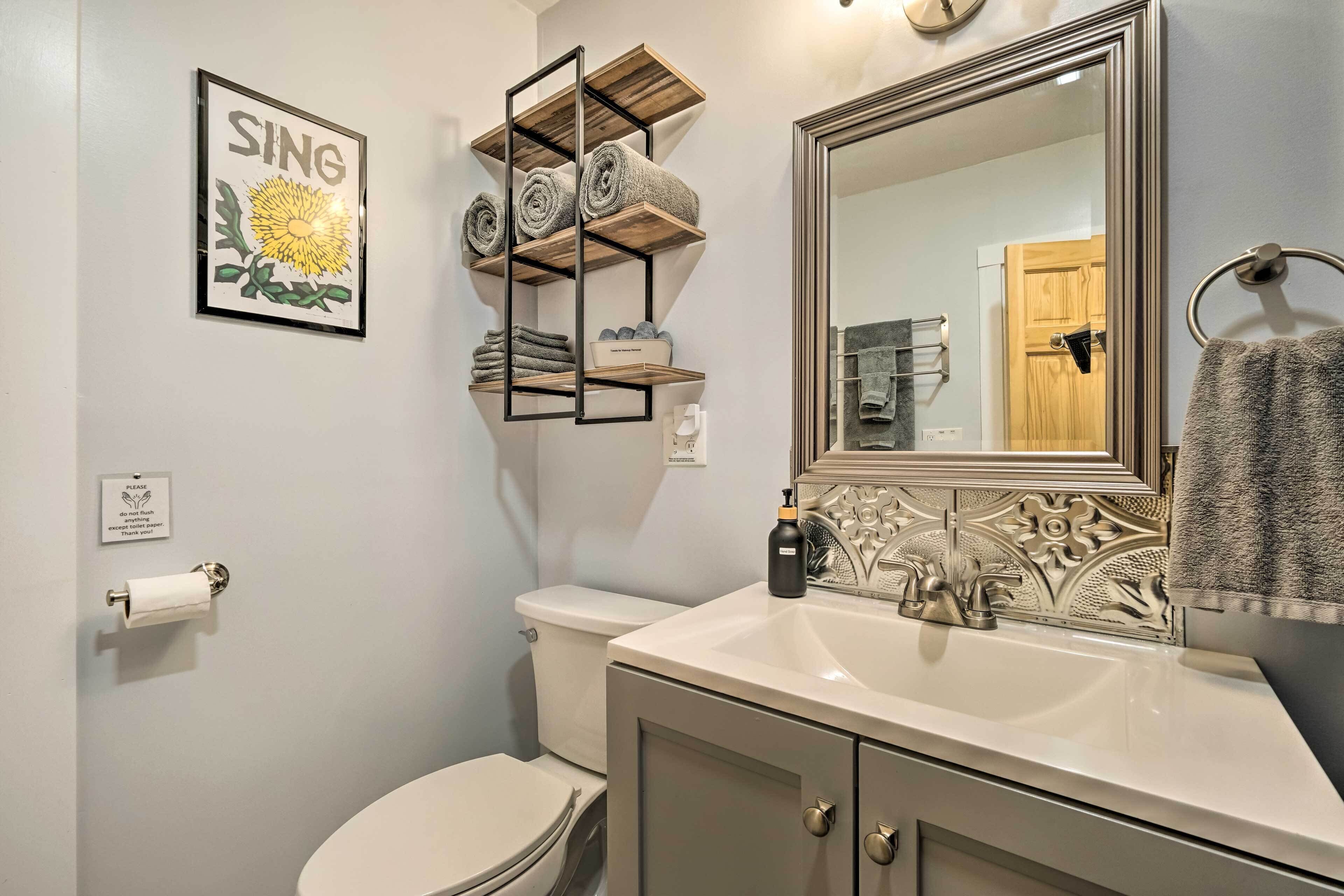 A bathroom with a toilet, sink, mirror, towel rack, and a shelf with towels.