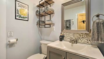 A bathroom with a toilet, sink, mirror, towel rack, and a shelf with towels.