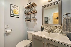 A bathroom with a toilet, sink, mirror, towel rack, and a shelf with towels. - Updated Vintage Apartment < 1/2 Mi to Main St (Keene)