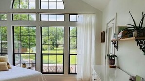 A bedroom with a large window, a bed, a dresser, and a view of a garden. - Lap Pool, Infrared Sauna & 1+ Acre in South Austin (Austin)