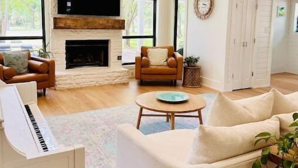 A spacious living room with a fireplace, a piano, and a large window offering a view of trees. - Lap Pool, Infrared Sauna & 1+ Acre in South Austin (Austin)