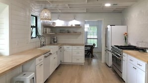 A modern kitchen with white cabinetry, wooden countertops, and a central island. There are built-in appliances, including a stove and oven, and a hanging light fixture. - Lap Pool, Infrared Sauna & 1+ Acre in South Austin (Austin)