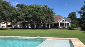 A swimming pool with clear water, surrounded by a well-maintained lawn and a large tree. - Lap Pool, Infrared Sauna & 1+ Acre in South Austin (Austin)