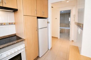 A kitchen with a stove, oven, refrigerator, and wooden cabinets. - Apartamento El Calón Playa - Lateral Luz (El Calón)
