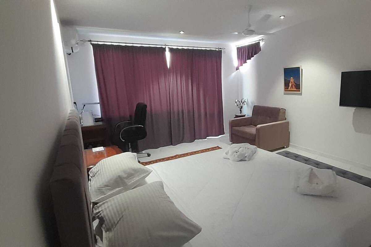 Una camera d'albergo con un letto, una scrivania, una sedia, una televisione e una finestra con tende.