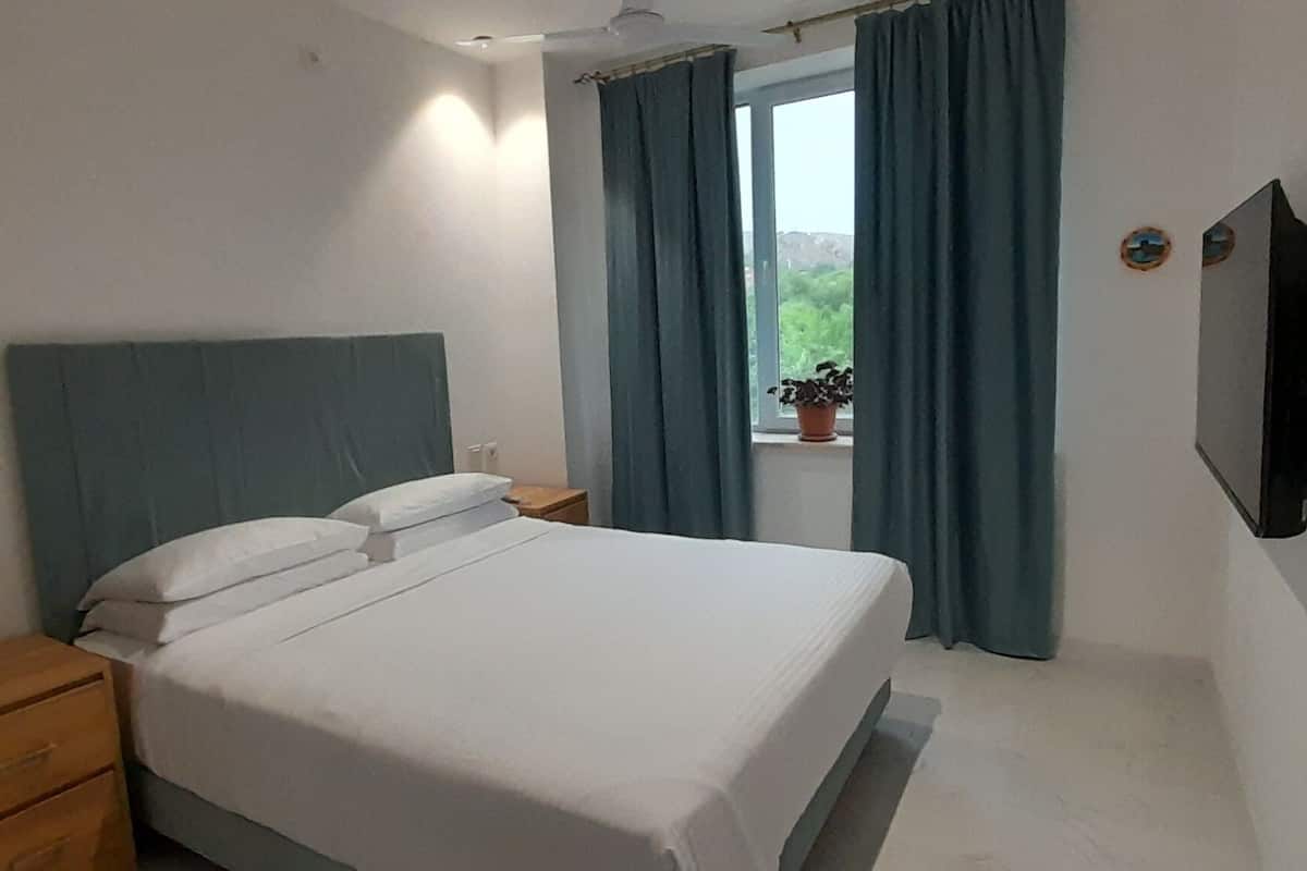 Una camera da letto con un letto, un comodino, una TV e una finestra con tende.