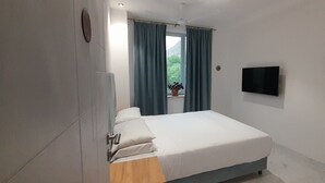 A bedroom with a bed, a TV mounted on the wall, and a window with curtains. - Areni Lodge (Areni)