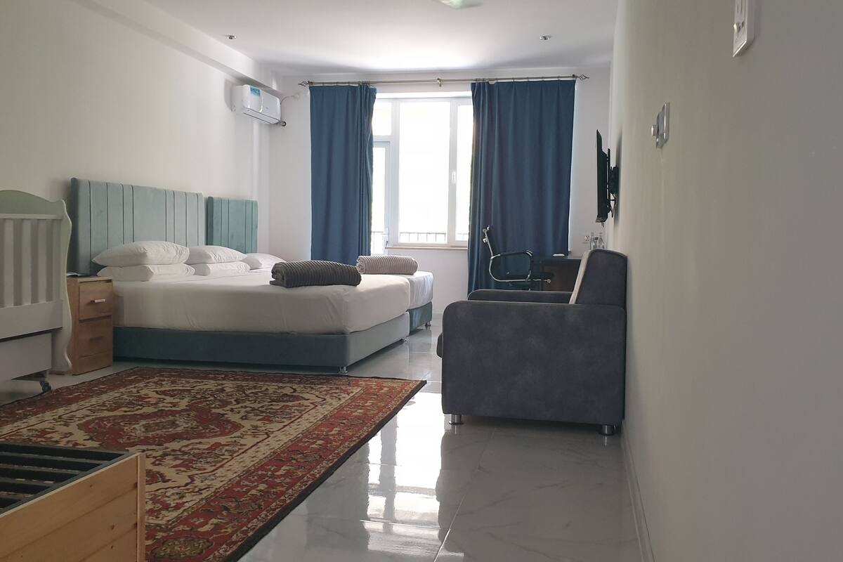 Una camera d'albergo con un letto, una scrivania, una sedia, una TV e una finestra con tende.