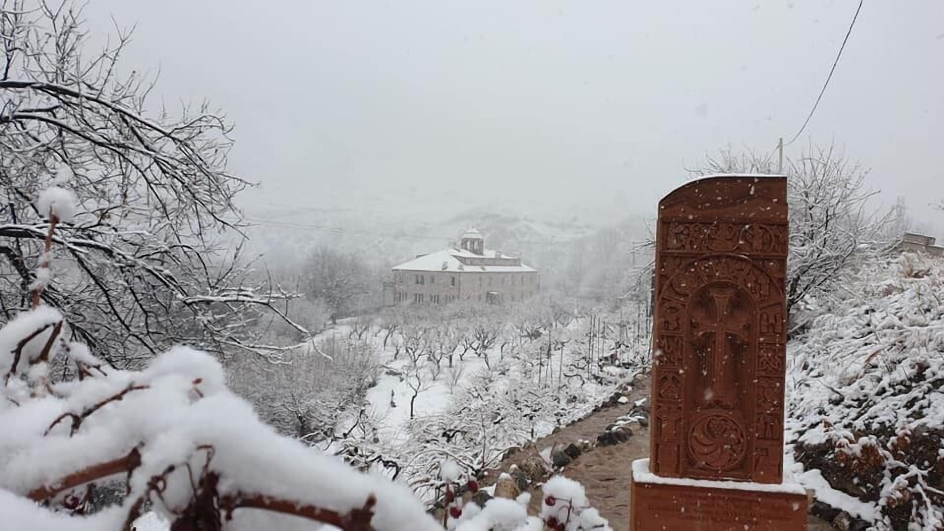 Un paisaje nevado con un edificio al fondo y un monumento en primer plano.