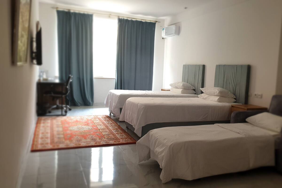 Una camera d'albergo con due letti, una scrivania, una sedia e un'ampia finestra con tende.