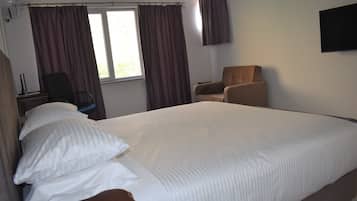 A hotel room with a large bed, two chairs, a desk with a lamp, and a window with curtains.