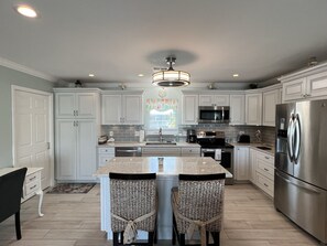 A modern kitchen with white cabinetry, stainless steel appliances, and a central island with two chairs.
