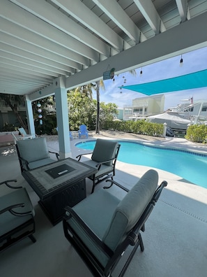 A covered outdoor seating area with lounge chairs and a pool.