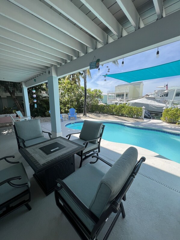 A covered outdoor seating area with lounge chairs and a pool.
