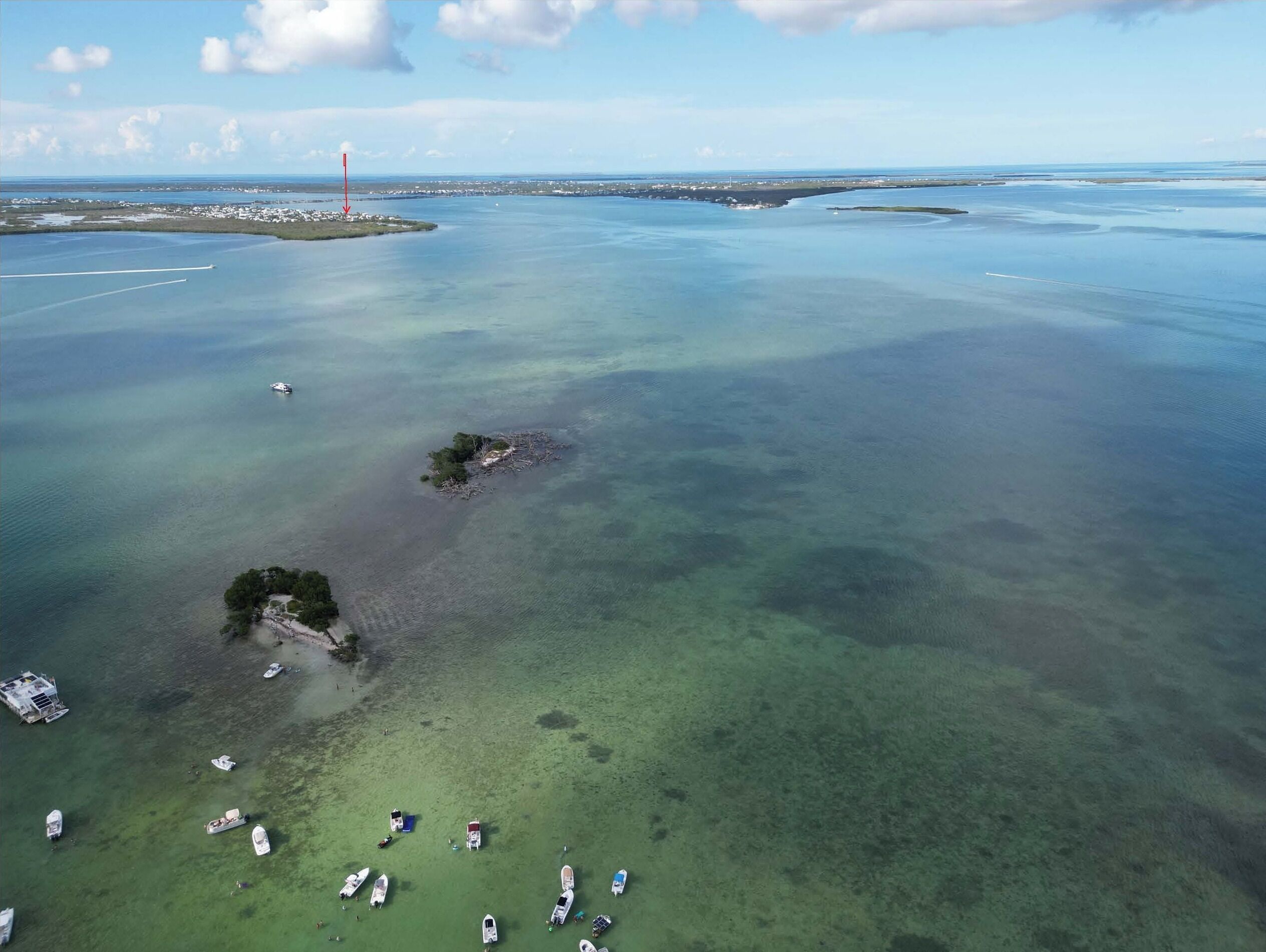 Une vue aérienne d’une zone côtière, avec des eaux cristallines, des bateaux et un phare visible au loin.