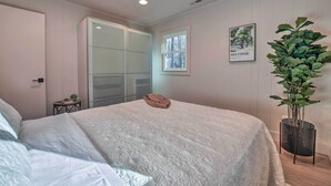 A bedroom with a large bed, a window, a door, and a potted plant. - Creekside Chalet With Deck < 7 Miles to Ski! (Maggie Valley)