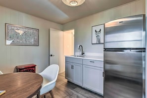 Una cocina moderna con armarios blancos, un refrigerador de acero inoxidable, un lavamanos y un comedor con mesa de madera y sillas blancas.