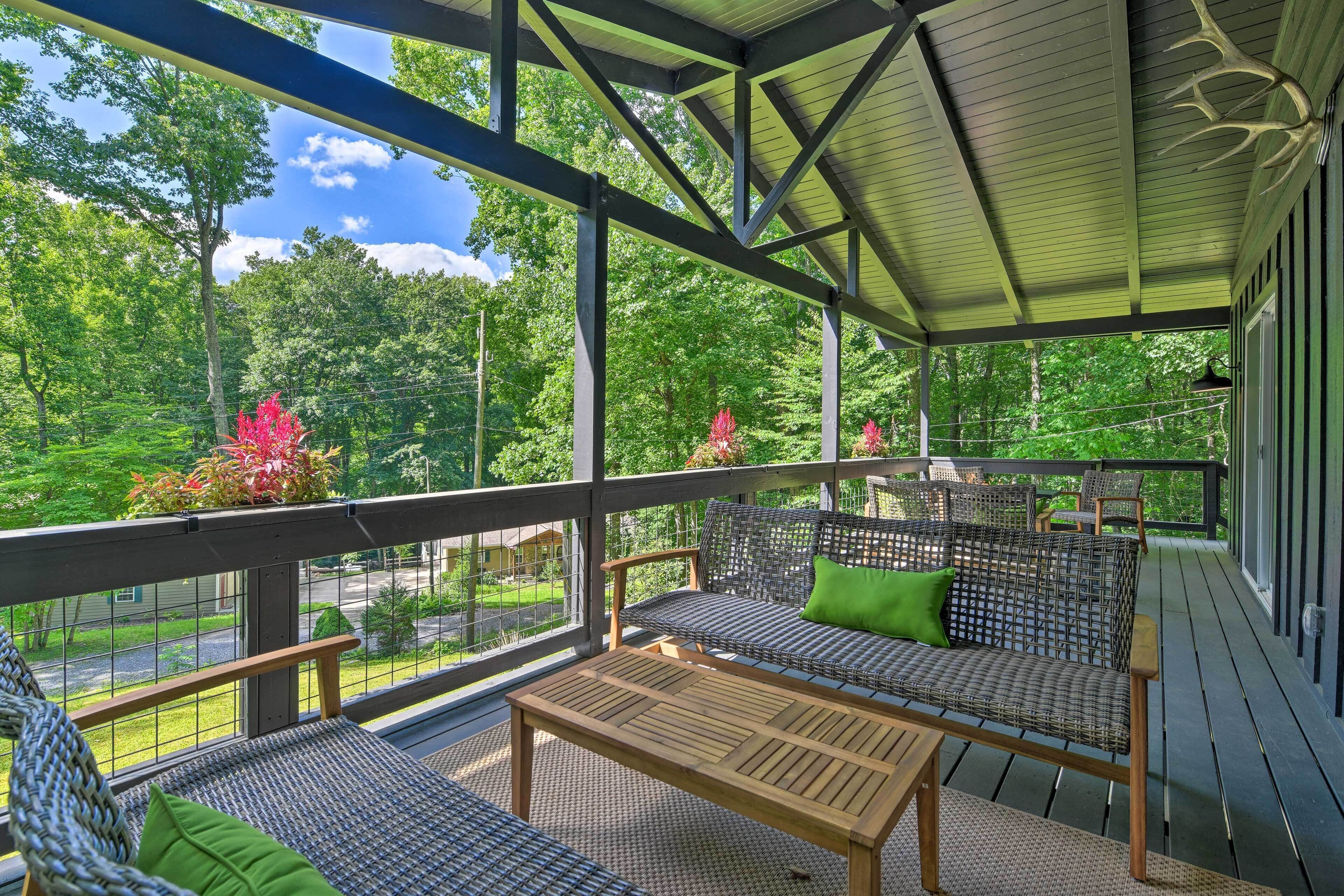 A covered outdoor seating area with wicker furniture and a wooden table, overlooking a lush green landscape.
