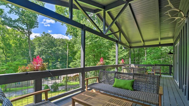 A covered outdoor seating area with wicker furniture and a wooden table, overlooking a lush green landscape. - Creekside Chalet With Deck < 7 Miles to Ski! (Maggie Valley)
