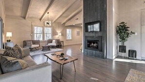 A spacious living room with a high ceiling, a fireplace, and a large window. - Creekside Chalet With Deck < 7 Miles to Ski! (Maggie Valley)