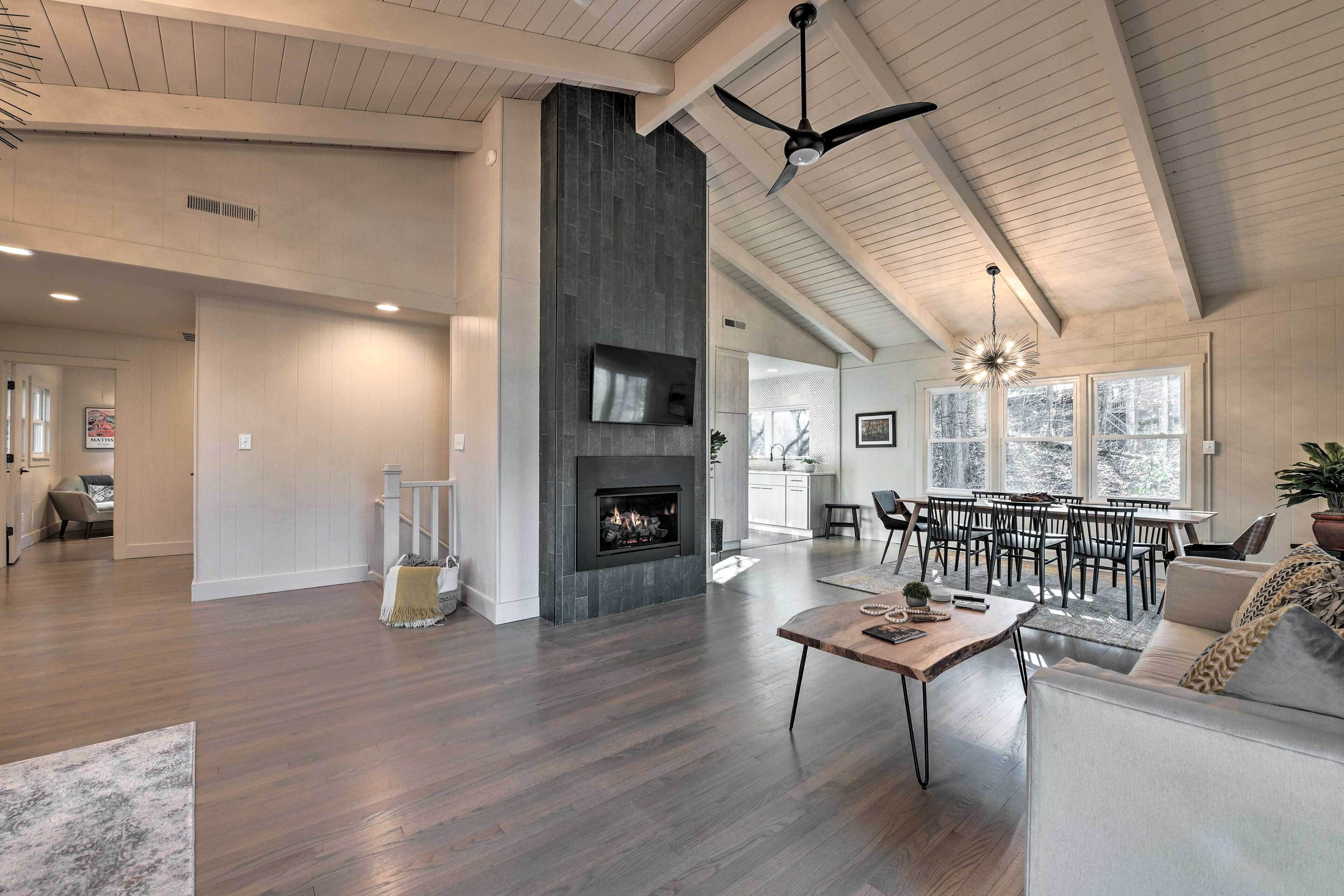 A spacious living area with a fireplace, wooden flooring, a dining area with a large table and chairs, and a ceiling fan.