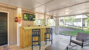 Un área de bar al aire libre con mostrador de bambú, dos taburetes de bar negros, un televisor montado en la pared y vistas del entorno.