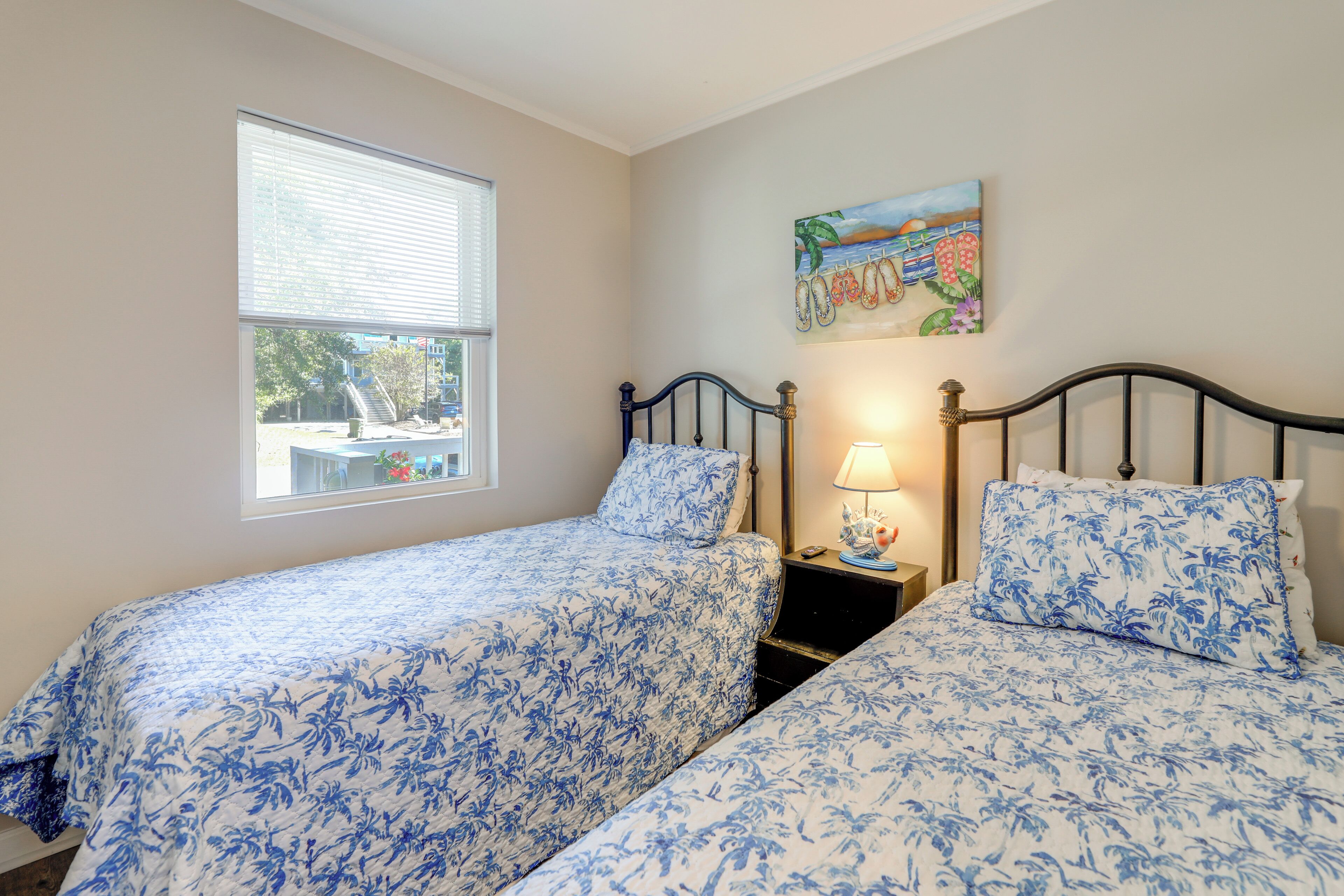 A bedroom with two beds, a window, a nightstand, and a painting.
